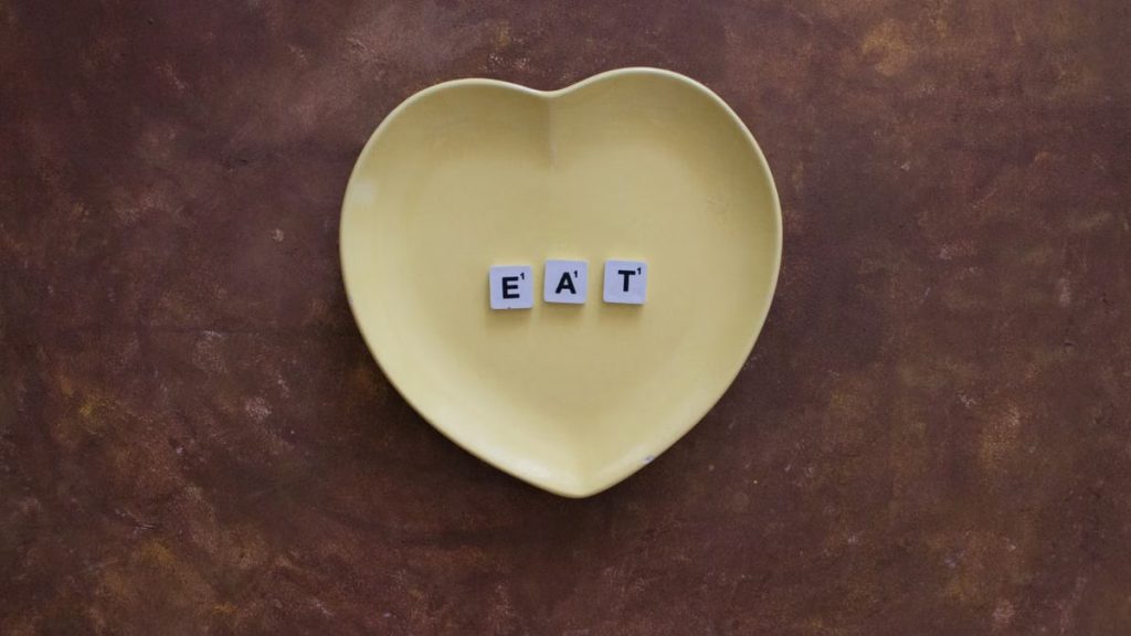 Yellow heart-shaped plate with letters spelling 'EAT' on brown background.