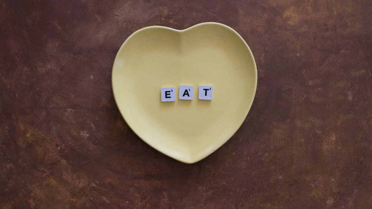 Yellow heart-shaped plate with letters spelling 'EAT' on brown background.